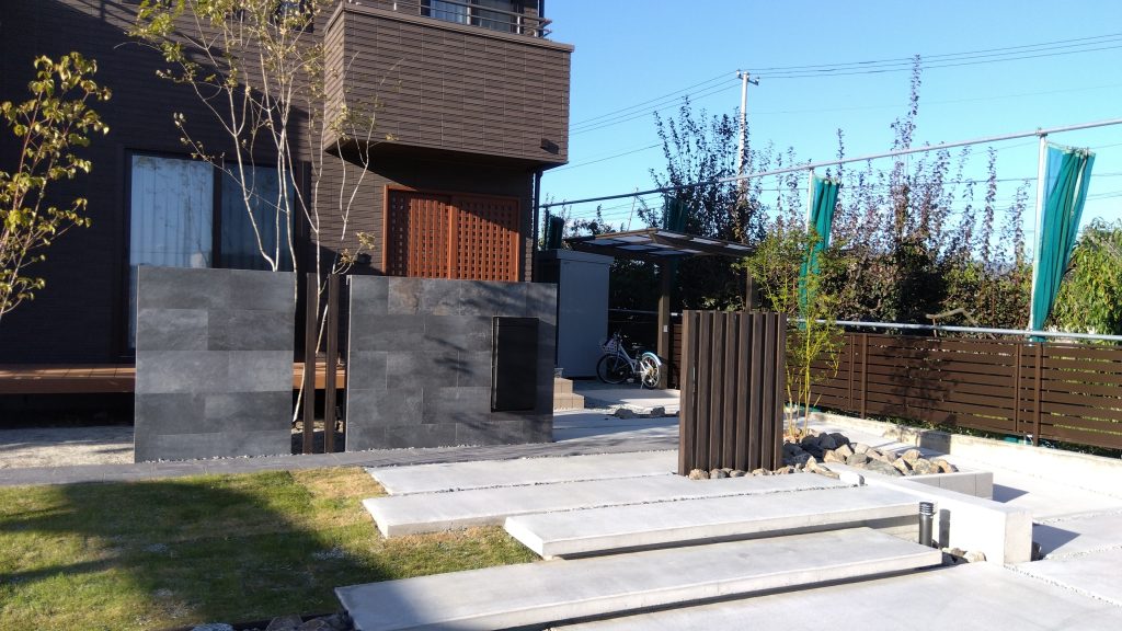 山梨県南アルプス市の外構施工例。黒タイル貼りの意匠壁と割栗石、雑木の庭が調和したナチュラルモダンなエントランス。