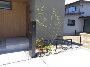 山梨県甲府市の外構施工例。LIXILの機能門柱とコンクリートカラー仕上げのアプローチ、雑木と割栗石が調和したナチュラルモダンな玄関周り。