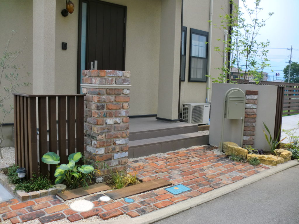 山梨県山梨市の外構施工例。アンティークレンガのレンガアプローチと木目調の角柱列柱、雑木が調和したナチュラルな玄関周り。
