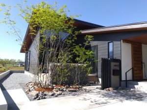 山梨県南アルプス市の外構施工例。蛇篭（ガビオン）と黒タイル貼りの意匠壁、雑木の庭が調和したナチュラルモダンなエントランス。
