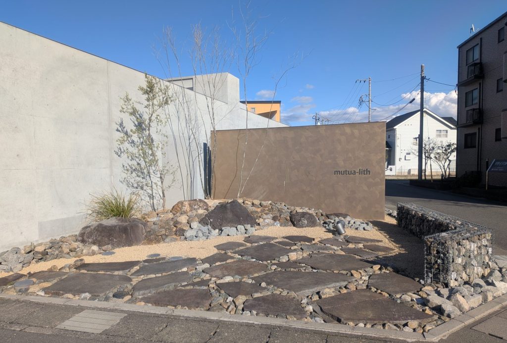山梨県甲府市のデザイナーズマンション「ミュートリス」の施工例。コンクリート壁の前に配置された蛇篭(ガビオン)とアガベ、割栗石のモダンなドライガーデン。