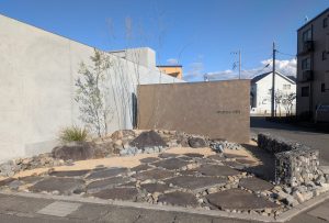 山梨県甲府市のデザイナーズマンション「ミュートリス」の施工例。コンクリート壁の前に配置された蛇篭（ガビオン）とアガベ、割栗石のモダンなドライガーデン。